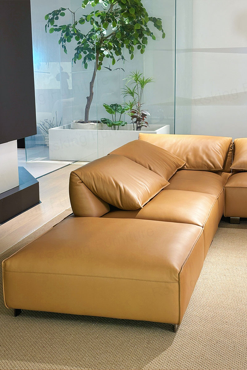 Close angled view of the caramel leather chaise area with broad cushions and a sloped back pillow