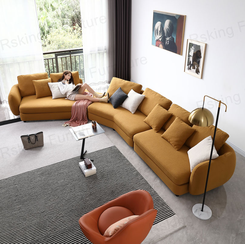 Elevated view of an ochre curved sectional sofa in a bright living room with a person lounging at one end