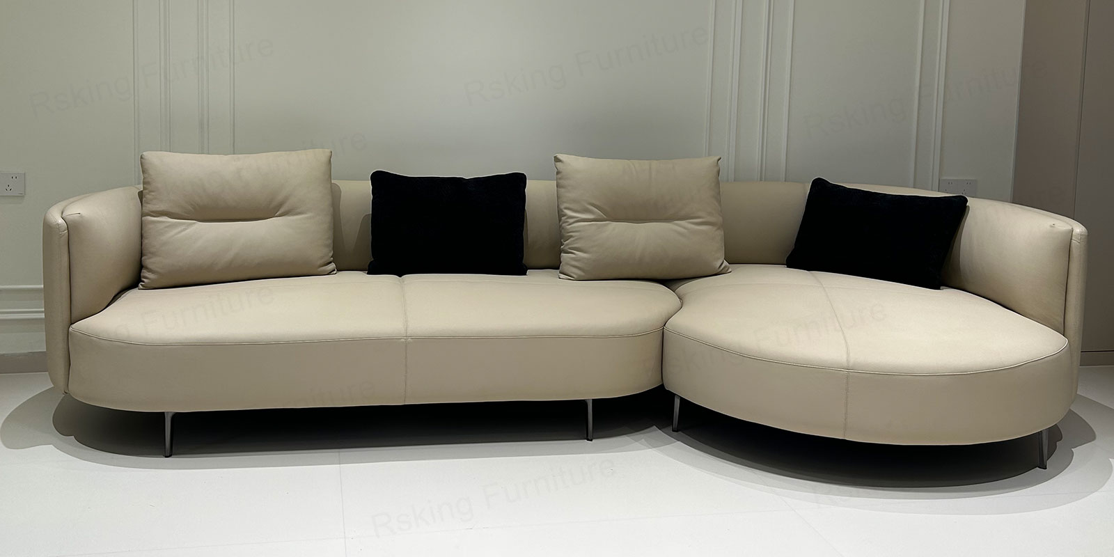 Front showroom view of the cream sofa with wraparound low back, rounded chaise and dark metal legs