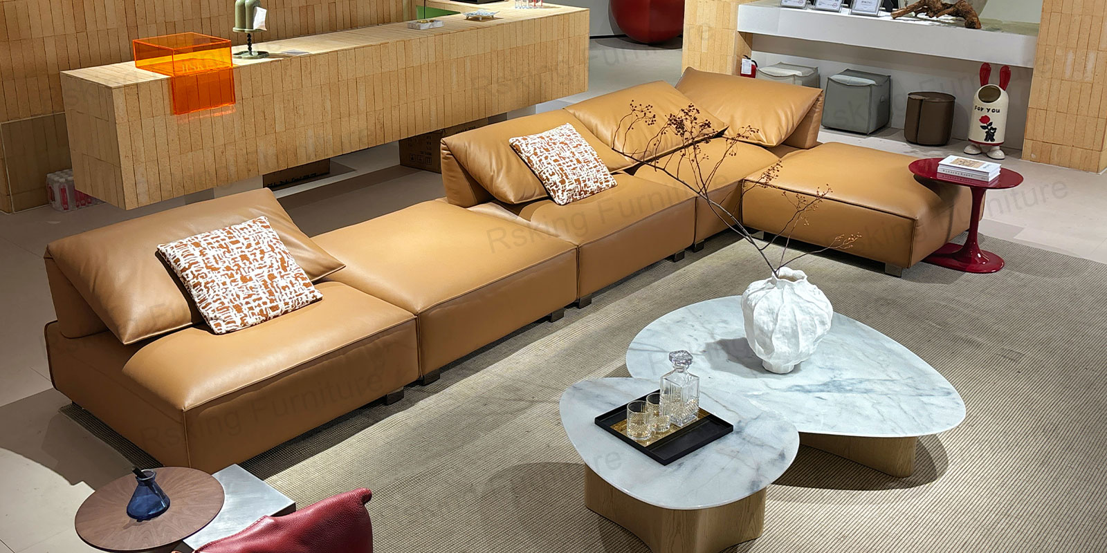Elevated showroom view of the caramel brown modular sofa and ottomans beside pale stone coffee tables