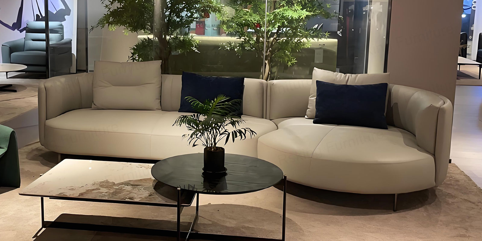 Rsking curved sofa with rounded chaise in a showroom beside stone and dark round coffee tables
