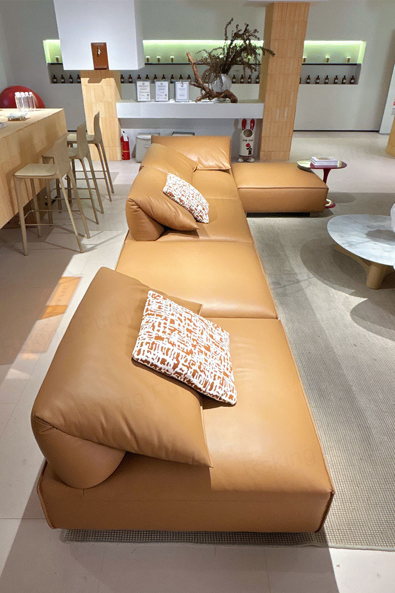 Side view along the caramel leather sofa showing open seating, patterned pillows and a projecting ottoman