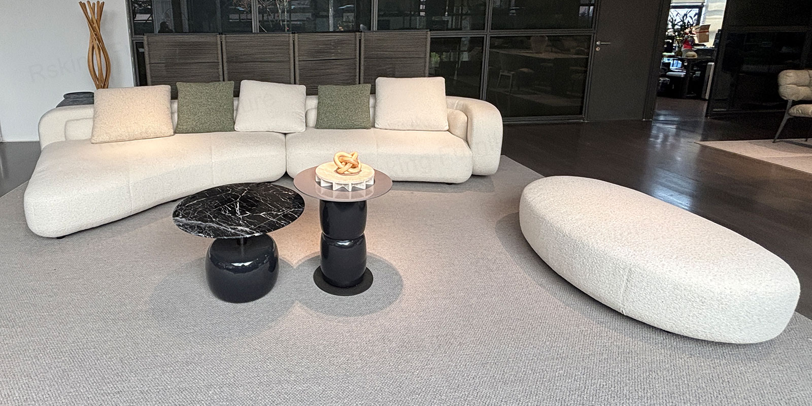RSK2560 cream curved sectional sofa with a separate oval ottoman and round coffee tables in a showroom