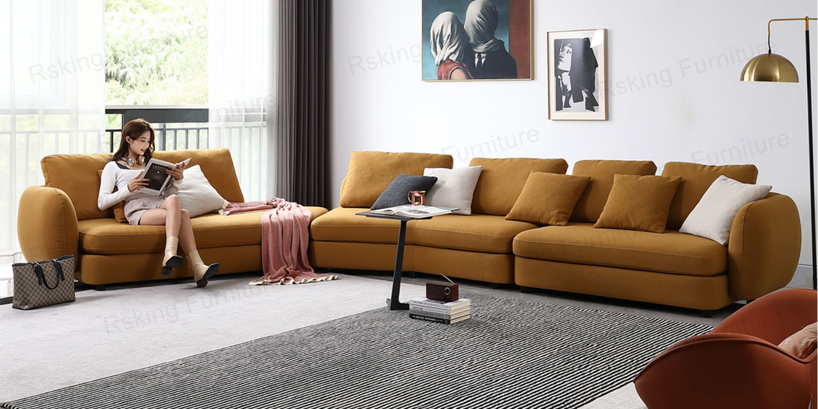 Ochre fabric sectional with rounded arms and layered pillows beside a window, with a person reading