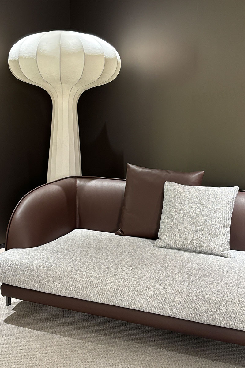 Detail of the rounded brown leather arm and light fabric seat cushion beneath a sculptural floor lamp