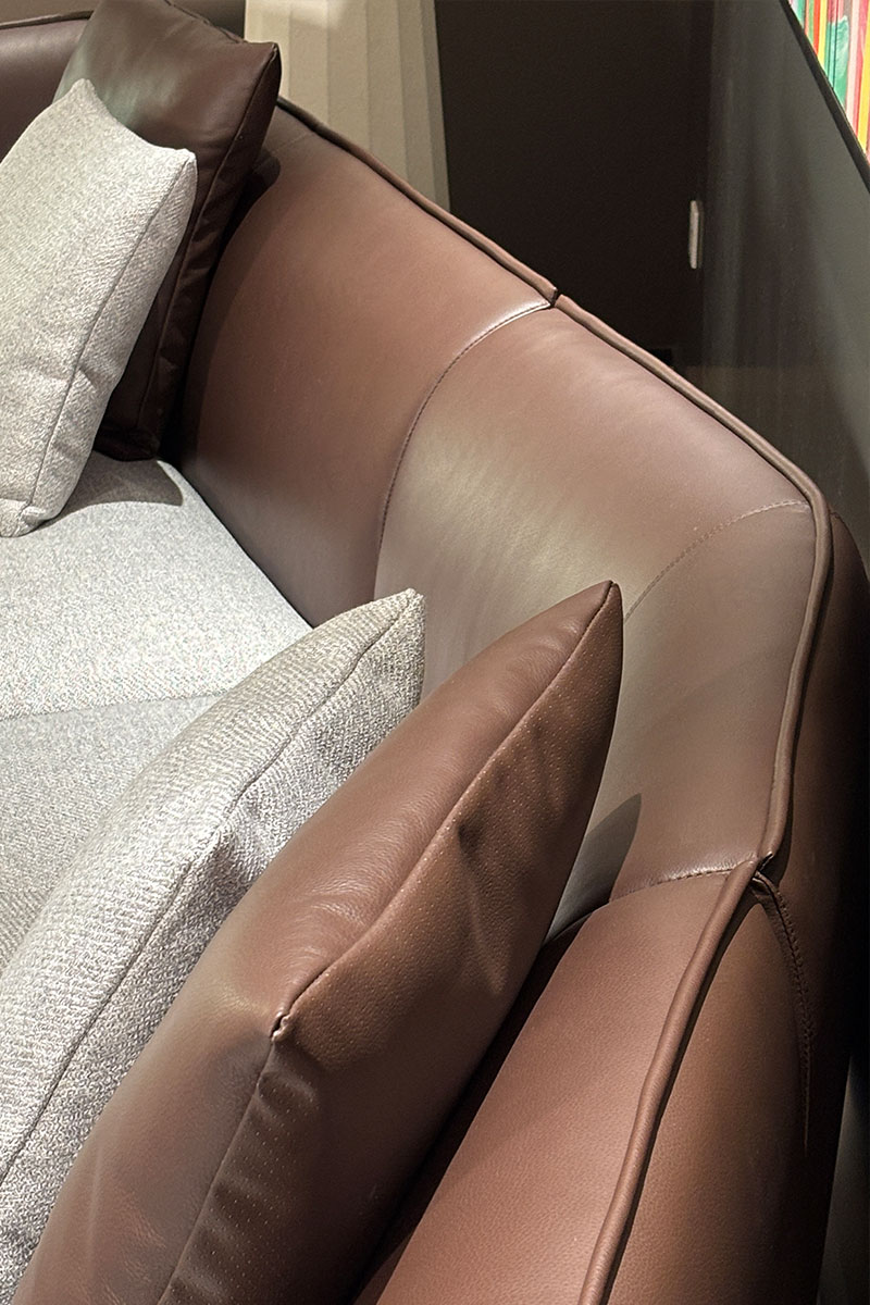 Close-up of the brown leather backrest showing curved seams, edge piping and contrasting woven pillows