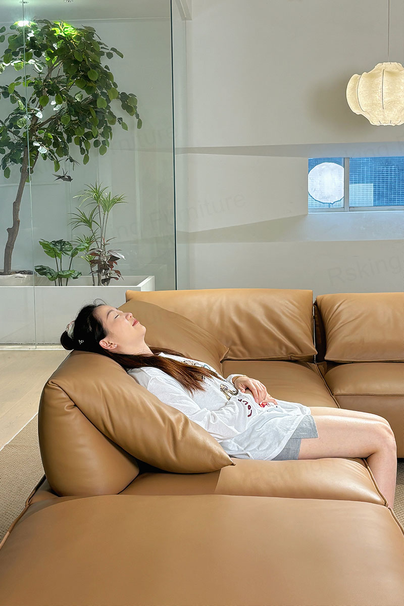 	A person resting against the angled pillow-style backrest of the caramel brown leather sofa
