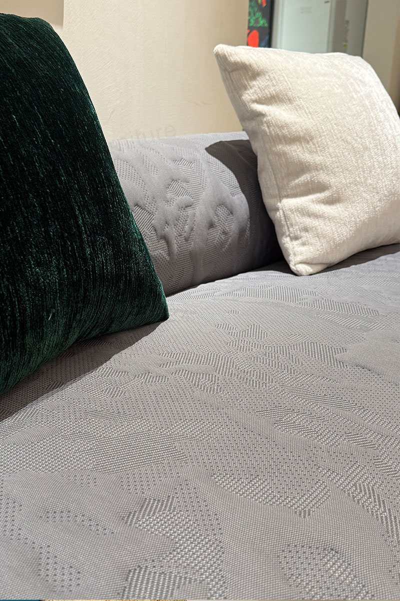 Close-up of raised jacquard texture on the gray sofa upholstery beside cream and deep green pillows